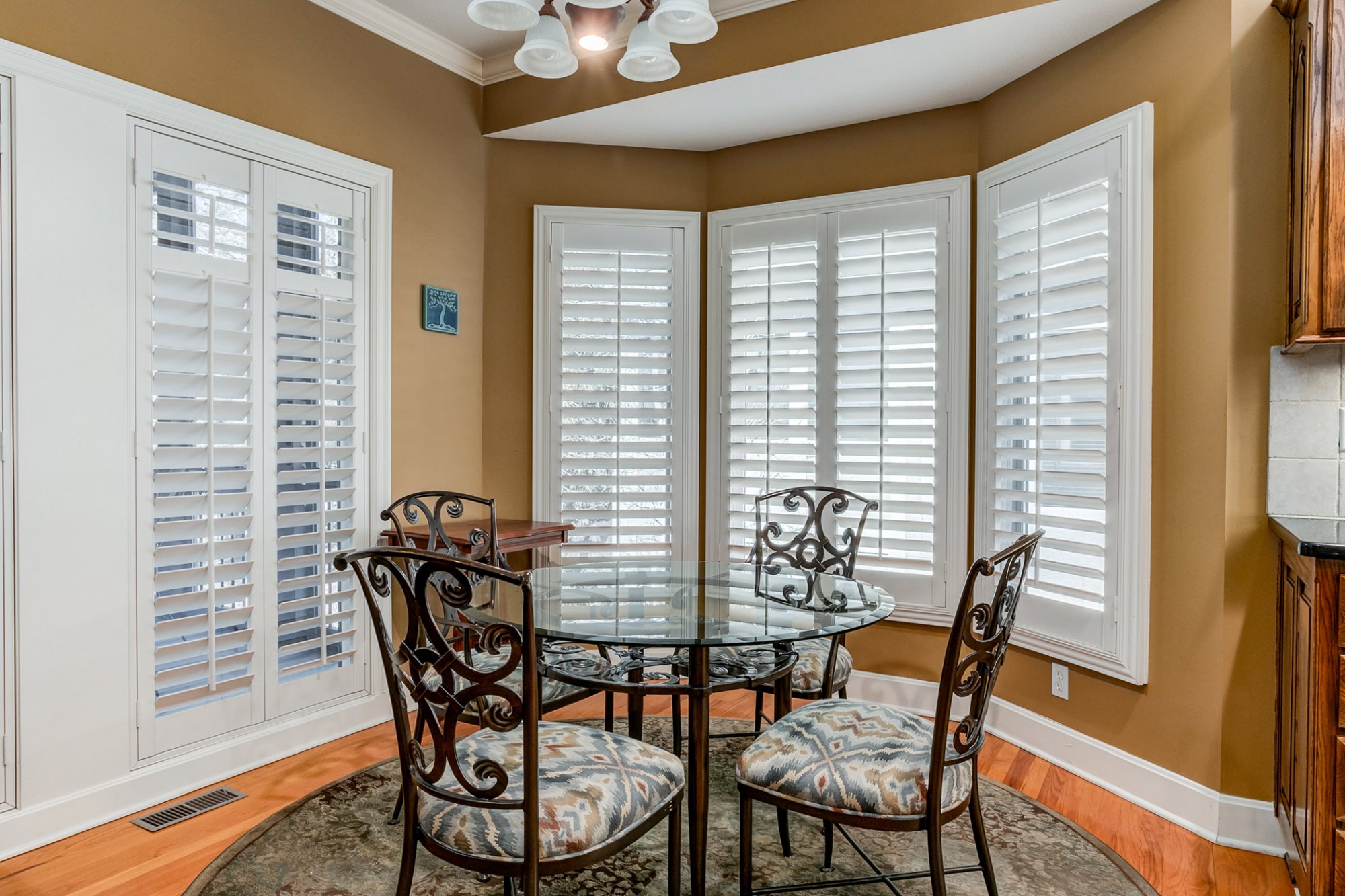 The bright & cheery breakfast area has a bay window plus a wall of windows, all featuring plantation shutters + a door opening to the screened porch.