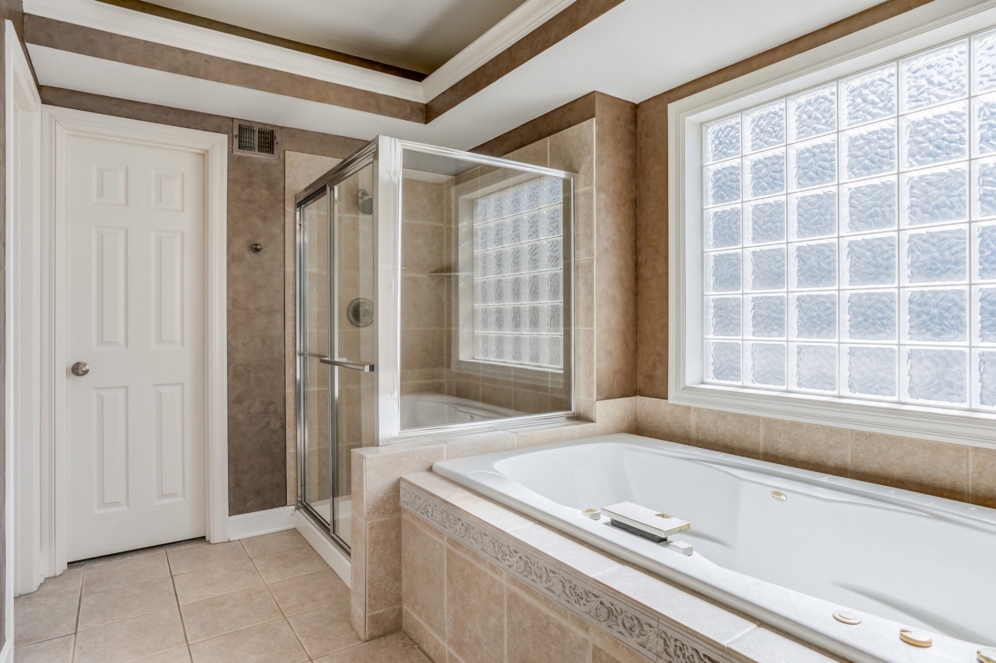 Relaxing Whirlpool tub with privacy glass block window above, separate walk-in shower, private water closet, large tile flooring & a walk-in closet.